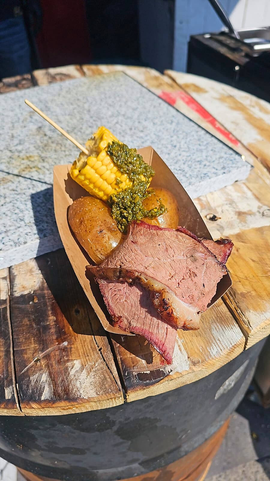 CARACAS Teller — Smoked Beef, gegrillter Mais am Spieß mit Chimichurri, Papas, serviert auf Holzfass