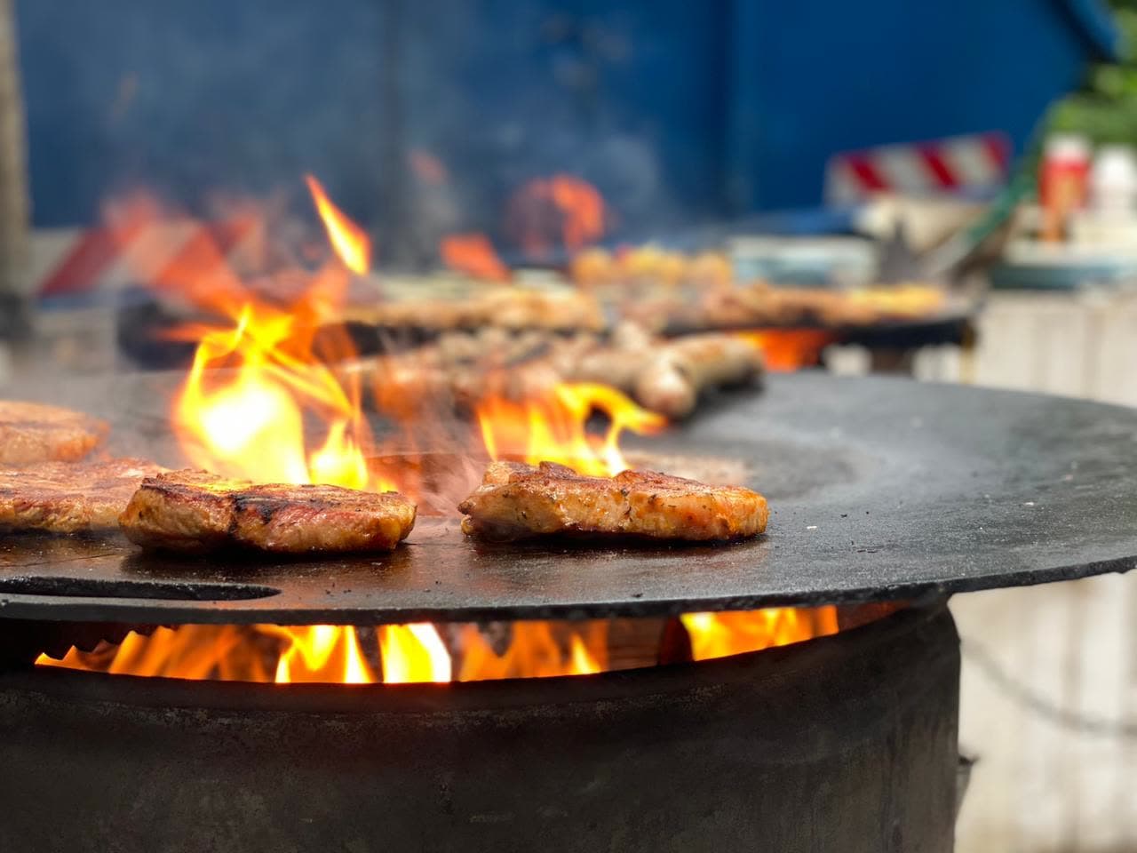 Offene Flamme unter der Feuerschale — Patties zischen auf der Plancha