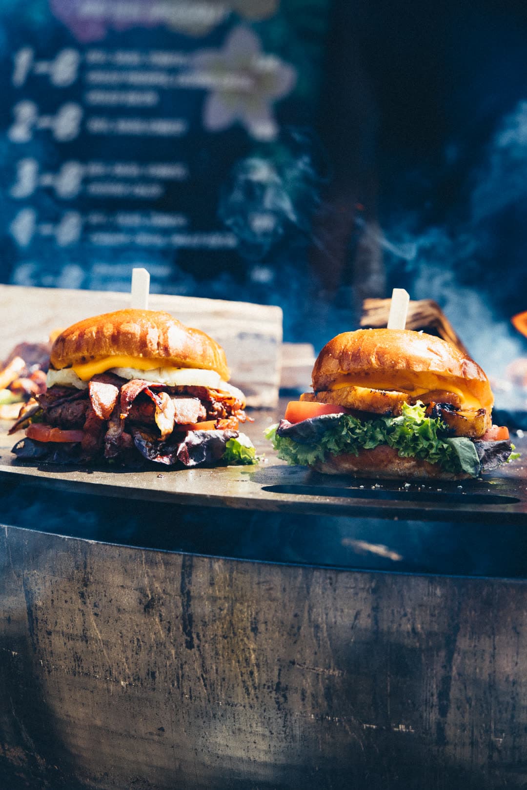 Fire Smash Burger — zwei frisch belegte Burger auf der Feuerschale mit FoodFighter-Menükarte im Hintergrund