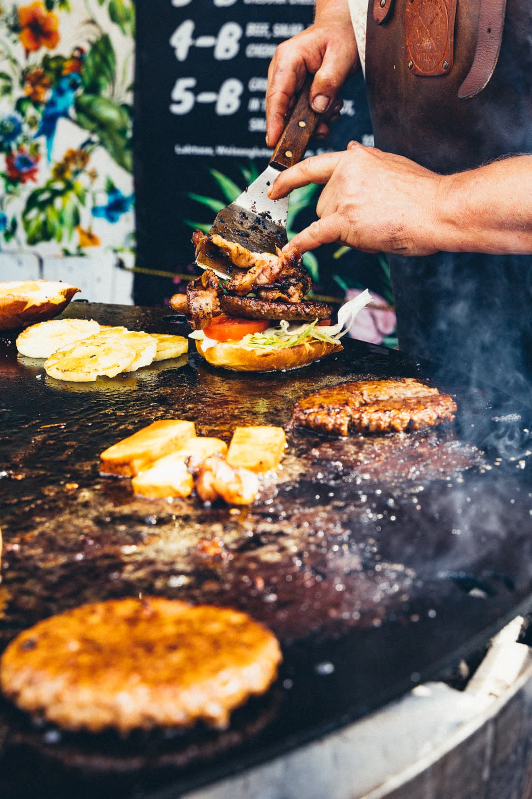 Hawaii 5B Burger wird von Hand auf der Plancha belegt — mit Ananas, Bacon, Tomate und Teriyaki-Patty
