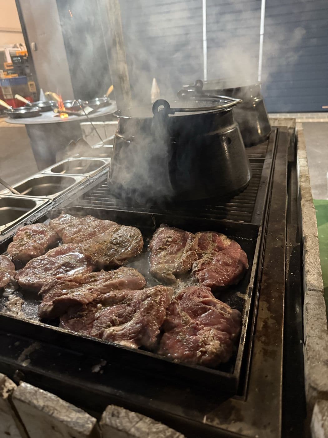 Schweinenacken auf der Feuerplancha, dahinter dampfen die ungarischen Töpfe